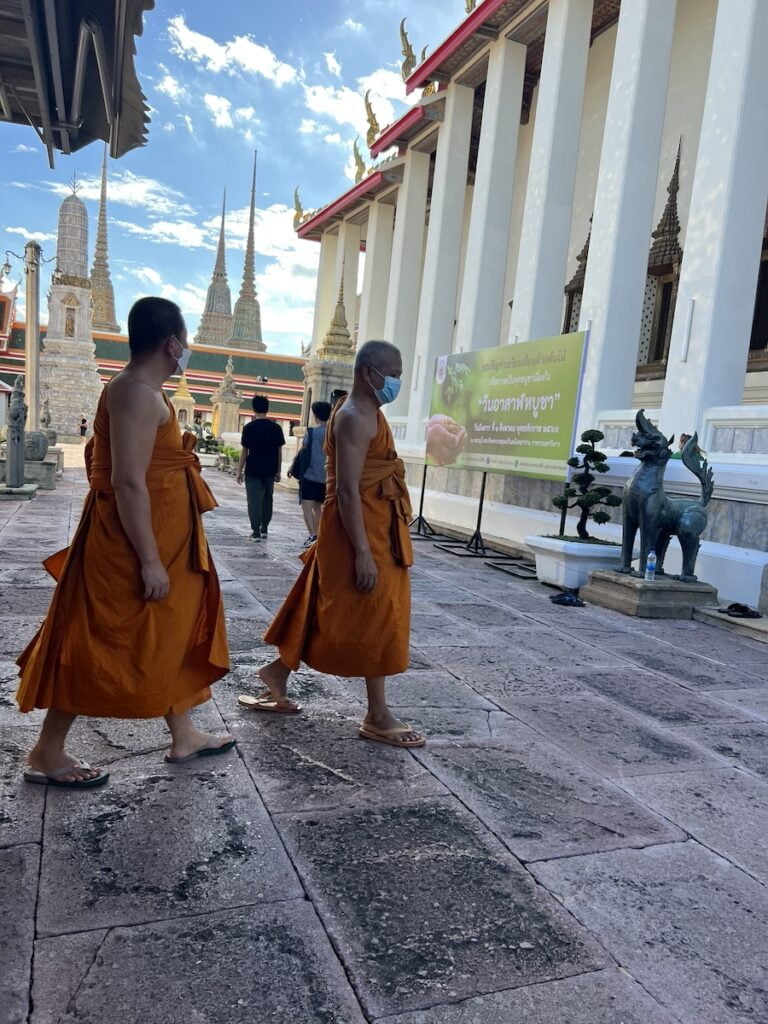 Two monks walking in front of a building in Thailand.