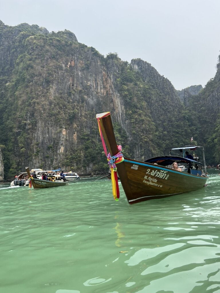 A group of boats in the water near a rocky cliff in Thailand.